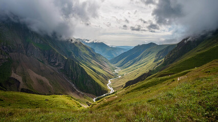 Wall Mural - Breathtaking Mountain Valley Landscape with Lush Green Slopes and Dramatic Rock Formations Under a Partly Cloudy Sky

