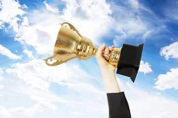 Wall Mural - woman holding golden trophy against sky, closeup