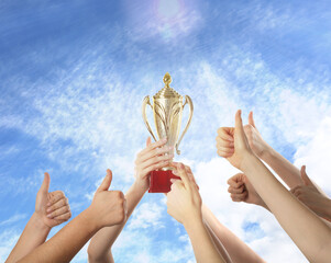 Wall Mural - woman holding golden trophy and people showing thumbs-up against sky, closeup