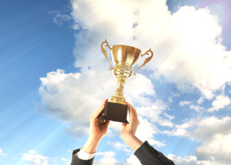 Wall Mural - man holding golden trophy against sky, closeup