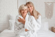 © Pixel-Shot - Happy young woman and her mother in bathrobes sitting on bed at home