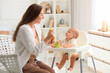 © Pixel-Shot - Mother feeding her baby in highchair at home