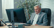 © ABCreative - Head of the company, elderly man with gray hair, dressed in an elegant jacket, conducts a remote conference over the Internet, using video camera presenting documents asking questions spreading hands