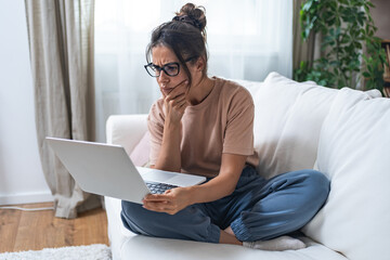 Young serious worried woman sitting at home on sofa using laptop computer research about earth environment pollution and dirty air. Self conscious ecology female trying to find information on internet