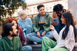 © Lomb - A diverse group of young friends chatting and laughing outdoors in the city. A happy multi-ethnic group of college students socializing and bonding, a concept of community and youth lifestyle.