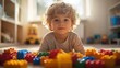 © Jamal - A young boy with curly blond hair lays on the floor surrounded by colorful building blocks. He looks directly at the camera with a thoughtful expression.