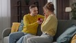 © kinomaster - Happy couple celebrating valentines day at home, man and woman sit on the sofa, man surprising woman with proposal gift jewelry ring, amazed expression.