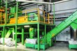 © Lidia - Industrial recycling plant with green machinery. Waste sorting facility with conveyor belts. Recycling process in factory setting. Large-scale recycling equipment in workshop.Waste material processing