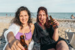 © Jorge - Two smiling women holding beer bottles relaxed on a beach
