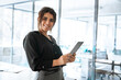 © Stock 4 You - Portrait of middle eastern businesswoman using tablet pc financial application standing in office. Smiling indian or latin hispanic business woman CEO holding digital pad computer, looking at camera.