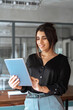 © Stock 4 You - 30s Latin Hispanic young professional business woman working on touchscreen computer. Middle eastern Indian businesswoman CEO holding digital tablet using tab application standing in office. Vertical