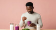 © Postmodern Studio - African male adult preparing berry smoothie with spinach in kitchen setting