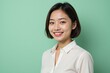 © SimpleDesignStudio - A Young East Asian Woman with Short Dark Hair Smiling Against a Soft Green Background in a Professional Setting, Exemplifying Confidence and Approachability
