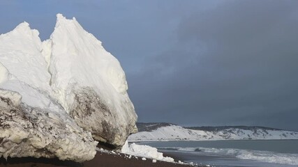 Wall Mural - wave breaking on winter beach by huge block of white snow
