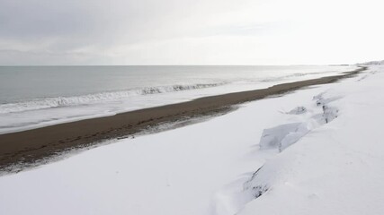 Wall Mural - frothy white waves breaking on snow-covered beach on bright winter morning