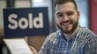 © sambath - A smiling broker with a client holding a signed contract in front of a 'Sold' sign.