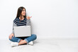 © luismolinero - Young caucasian woman with a laptop sitting on the floor isolated on white background pointing to the side to present a product