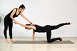 © TRAVELARIUM - Two young women in black outfits practice yoga on gray mat in bright studio. One assists other in achieving balanced pose, creating calm and focused atmosphere