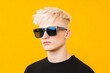 © Leo Rohmann - Stylish young man with platinum blonde hair wearing sunglasses against bright yellow and orange background exuding confidence in bold minimalistic style