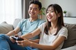 © SimpleDesignStudio - Young Asian Couple Enjoying Video Games Together at Home on a Comfortable Sofa in a Bright Living Room, Smiling and Engaged in Playful Competition