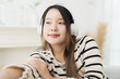 © amorn - Woman, happy smiling, young Asian woman on sofa listening to music with headphones, playlist or radio in home. Enjoy face of woman relax on sofa and streaming song or album at home