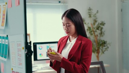 Fototapete - Confident Asian businesswoman presenting strategic project details, wearing red jacket, working in modern collaborative corporate office with professional demeanor
