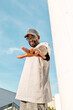 © Anna Zhukkova - Stylish young African American man wearing casual streetwear, sunglasses and Hat while standing outdoors and reaching out hand against bright blue sky, exuding confidence and positive on sunny day