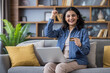 © Tetiana - Enthusiastic woman celebrates online shopping success with credit card and laptop on the sofa.