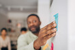 © Maskot - Hand of male entrepreneur sticking adhesive note on whiteboard in meeting room at office