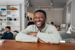 © Maskot - Portrait of smiling male creative professional leaning on table with arms crossed in office