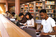 © Maskot - Male and female university students learning while sitting at desk in library
