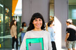 © Maskot - Portrait of smiling female student standing with book and file folder at college campus