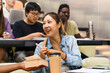 © Maskot - Smiling female student looking at friend holding book while sitting in lecture hall