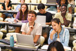 © Maskot - Multiracial male and female students sitting at desks in university lecture hall