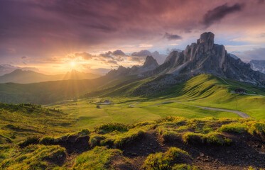 Wall Mural - Lush green valley, beautiful alpine mountains during colorful sunset in summer. Passo Giau, Dolomites, Italy. Landscape with green meadows, road, high rocks and pink sky with clouds at golden sunset