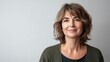 © scrdy - Attractive middle-aged woman with stylish wavy hair and a warm, inviting smile poses in front of neutral background.