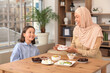 © Pixel-Shot - Happy Muslim mother and her daughter sitting at table with traditional sweets in living room. Eid al-Fitr celebration