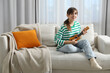 © New Africa - Happy woman playing ukulele on sofa at home