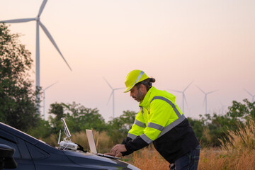 Fototapete - Engineer working on laptop in front of wind turbines for checking wind turbines of the field during beautiful sunset. Alternative energy concept.