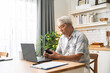 © winnievinzence - Asian senior man checking on mobile phone while working with laptop and document at home. Retired grandfather managing financial payment after retirement