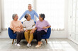 © artitwpd - Four happy Asian senior friends enjoying laughter and bonding in a cozy home setting. Elderly man and three women sitting on a couch, embracing companionship, joy, and a healthy social lifestyle.