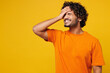 © ViDi Studio - Young sad confused shocked Indian man wear orange t-shirt casual clothes put hand on face facepalm epic fail mistaken omg gesture isolated on plain yellow background studio portrait Lifestyle concept
