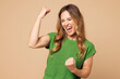 © ViDi Studio - Young overjoyed woman she wear green t-shirt casual clothes doing winner gesture celebrate clenching fists say yes isolated on plain pastel light beige background studio portrait. Lifestyle concept.