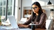 © goodskin - 'Focused Young Hispanic Woman with Glasses Working on Her Computer in a Modern Office'
