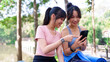 © Pichsakul - Two young Asian women sitting on a park bench, looking at a smartphone and resting after an outdoor workout