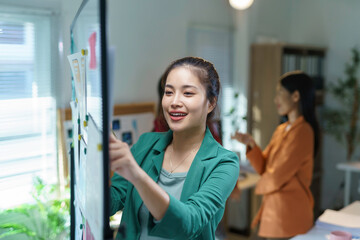 Wall Mural - professional asian businesswoman collaborating with team, placing sticky notes on glass board during