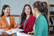 © amnaj - Three young businesswomen are smiling and discussing financial report during a meeting in a modern office, showing teamwork and collaboration