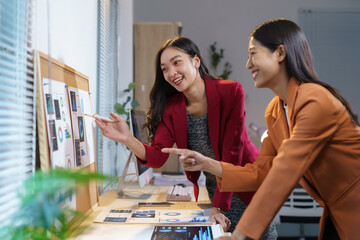 Wall Mural - professional asian businesswomen reviewing marketing strategies, gesturing toward charts in contempo