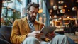 © angelmaxmixam - Man using tablet. Man reading on his device while sitting in a chair. He is in a cafe with soft light. Tech use.