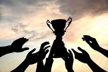 Wall Mural - silhouettes of people reaching for trophy against sky, closeup